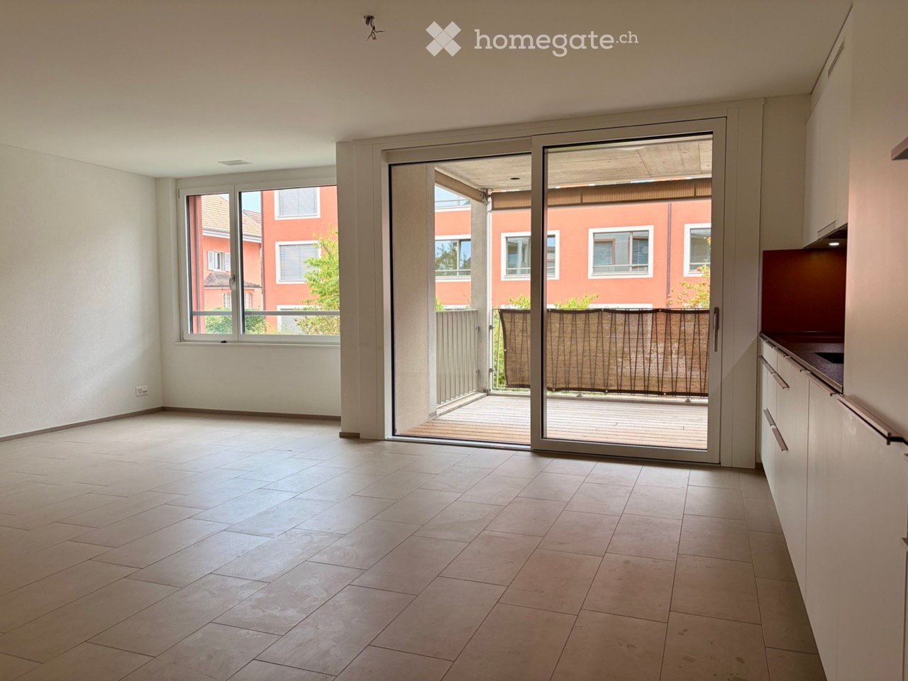 Empty room with tiled floor, large sliding glass door leading to a balcony, and a window with a view of a red building.
