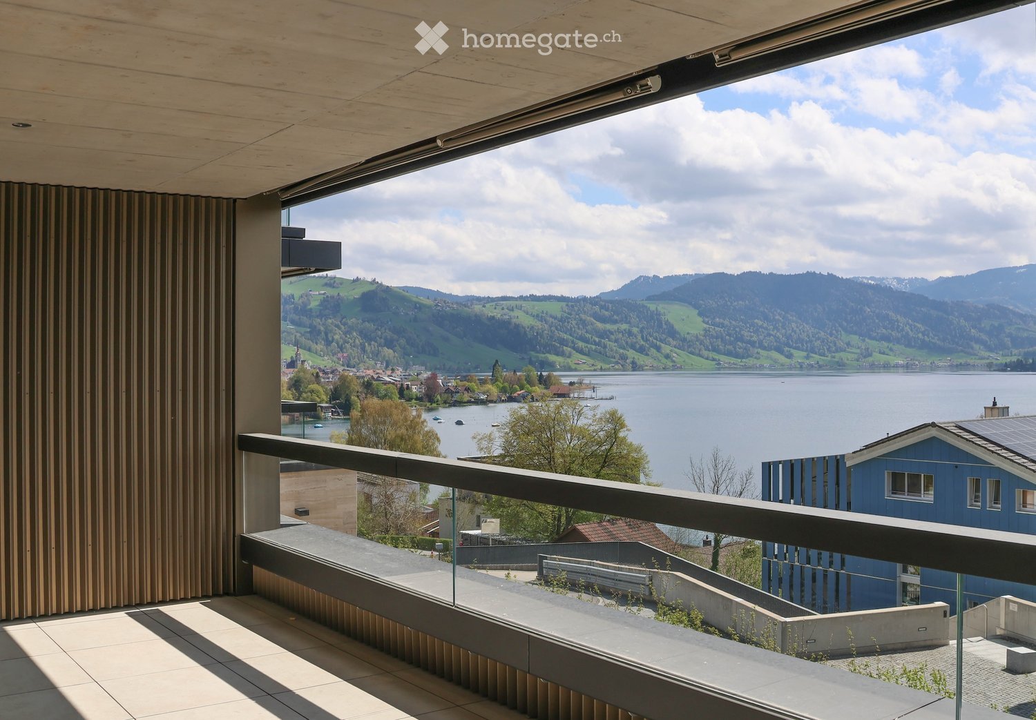 Balcony with a modern design, overlooking a scenic lake and distant mountains, with a cityscape visible in the distance.