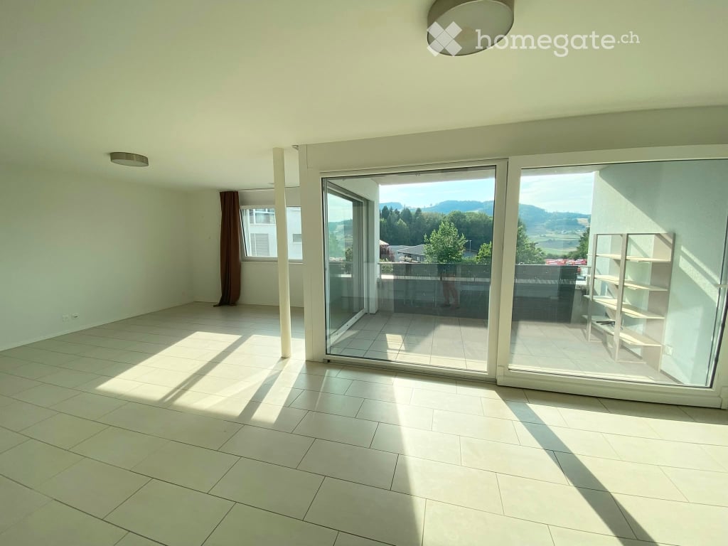 Bright, empty room with large sliding glass doors leading to a balcony, tiled floor, and a scenic mountain view.