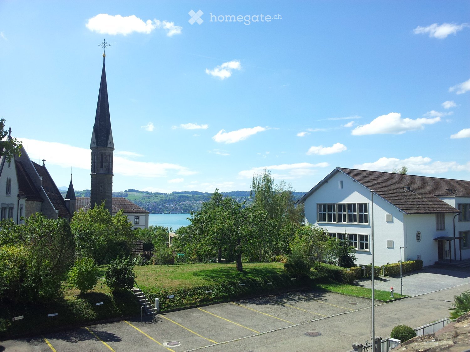 A church with a tall spire and a modern building next to it, surrounded by greenery and a parking lot.