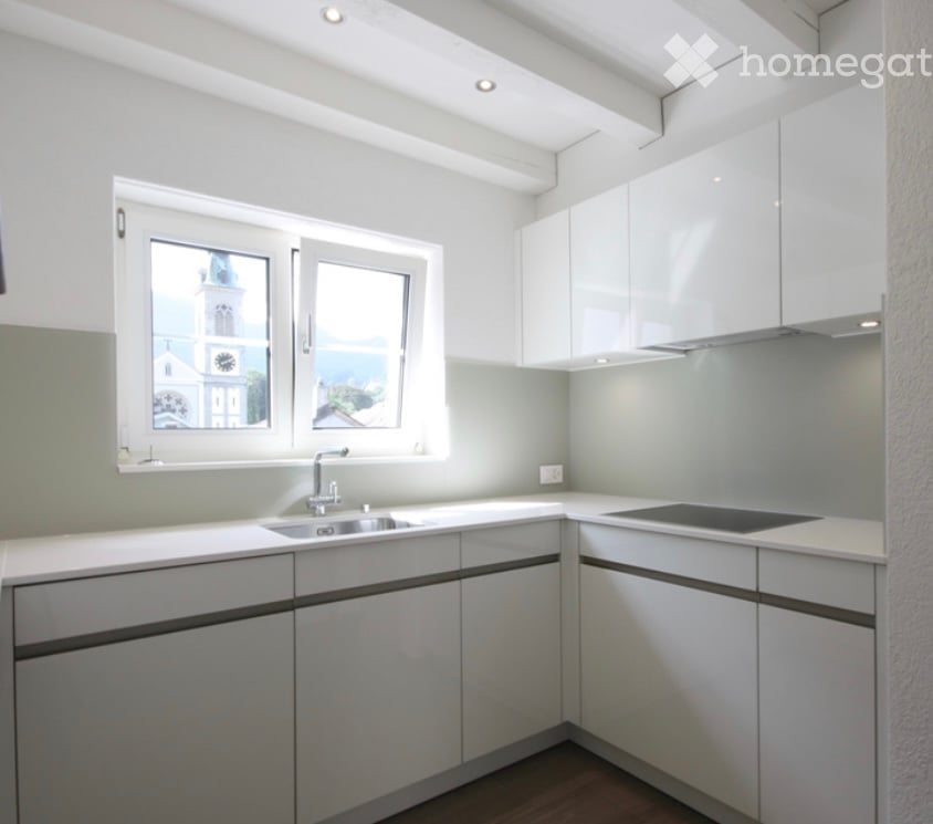 Modern kitchen with white cabinets, a sink, a stove, and large windows offering a view of a church tower.