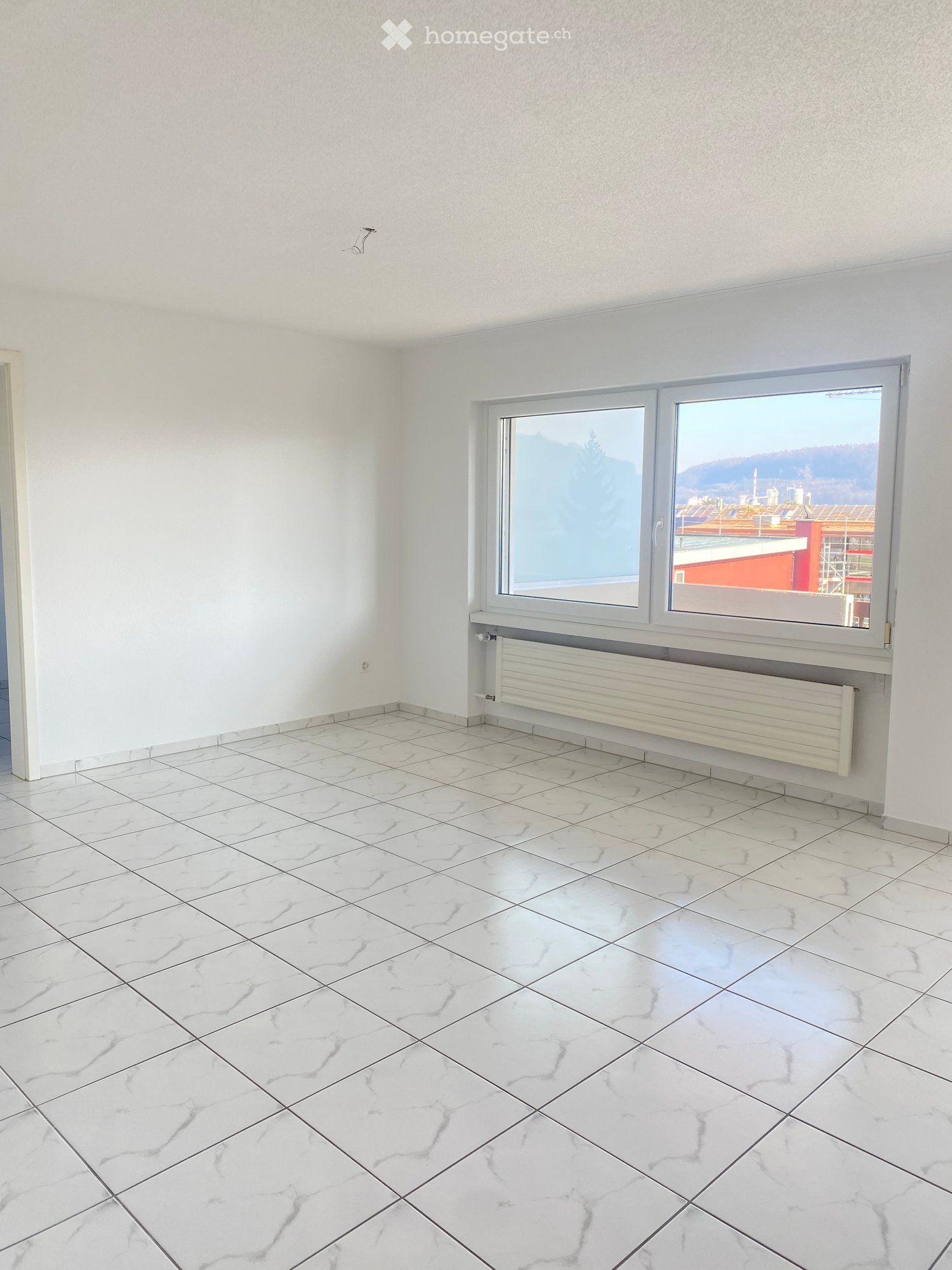 Empty room with white marble tiles and large windows offering a view of the cityscape.