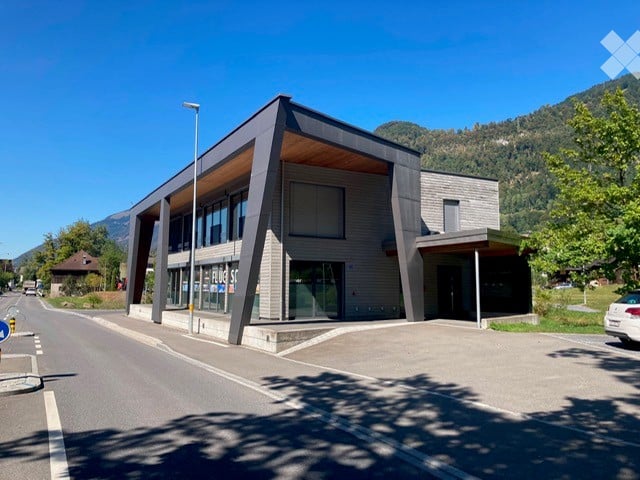 Modern building with a sleek, angular design and large glass windows, situated on a street with a clear view of surrounding mountains.