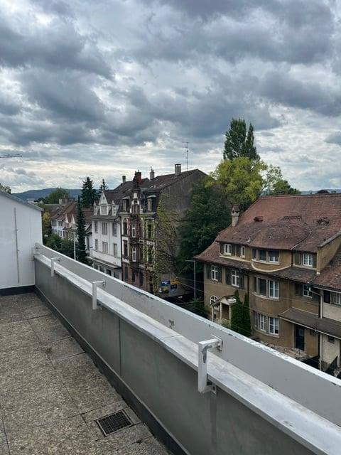 Balcony with white railing overlooking a residential area with multi-story houses and trees.