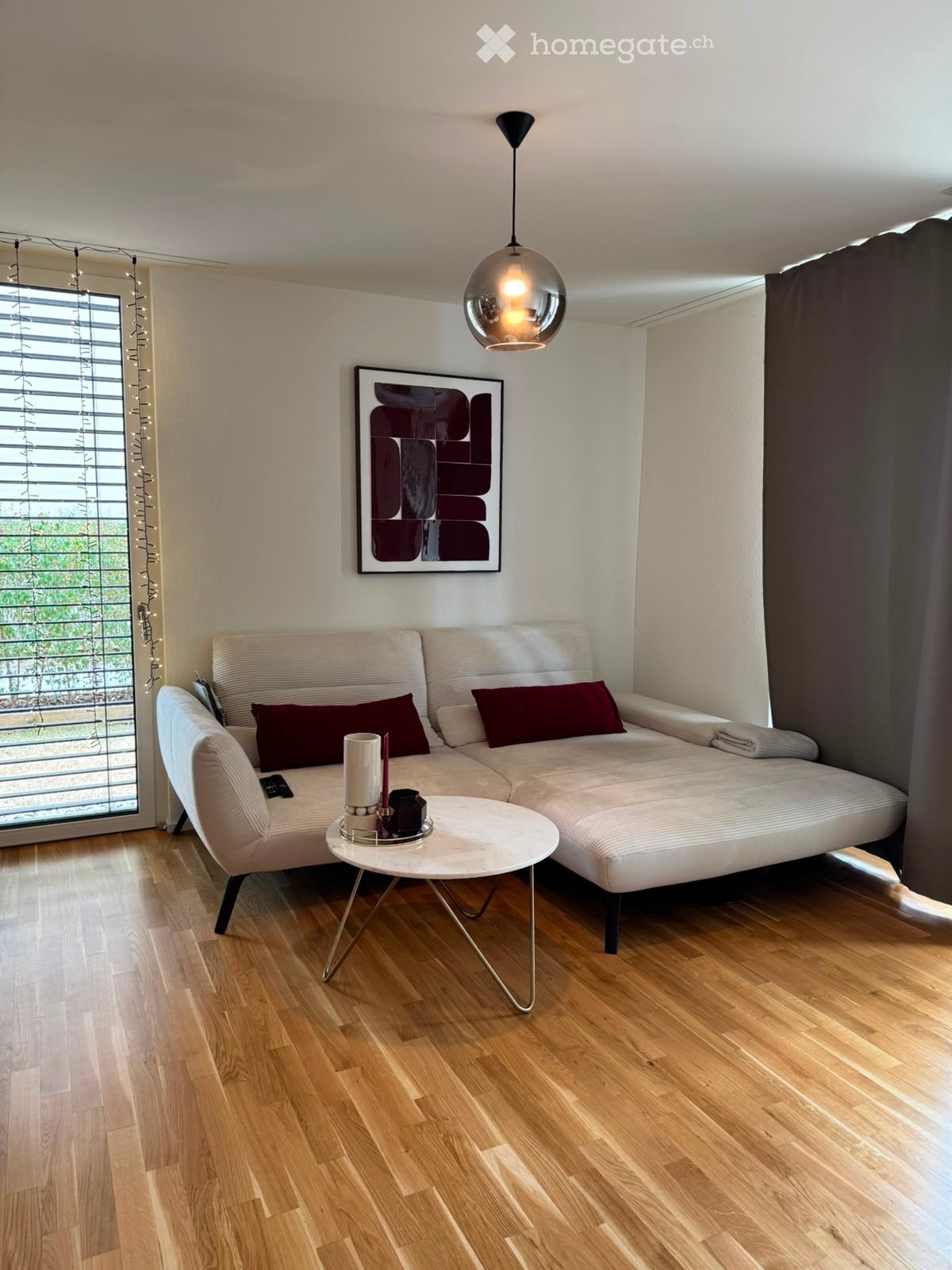 Modern living room with a white sectional sofa, a small round coffee table, a hanging pendant light, and a large abstract picture frame on the wall.