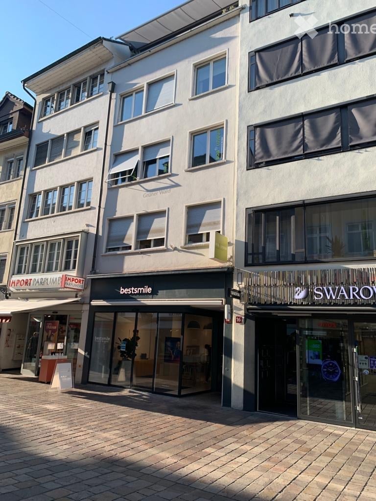 Multi-story commercial building with large glass storefronts, including 'bestsmile' and 'SWAROVSKI' signage, and a brick-paved sidewalk.