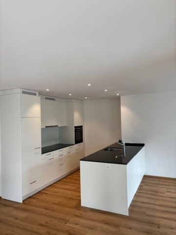 Modern kitchen with white cabinets, black countertops, and a wooden floor.