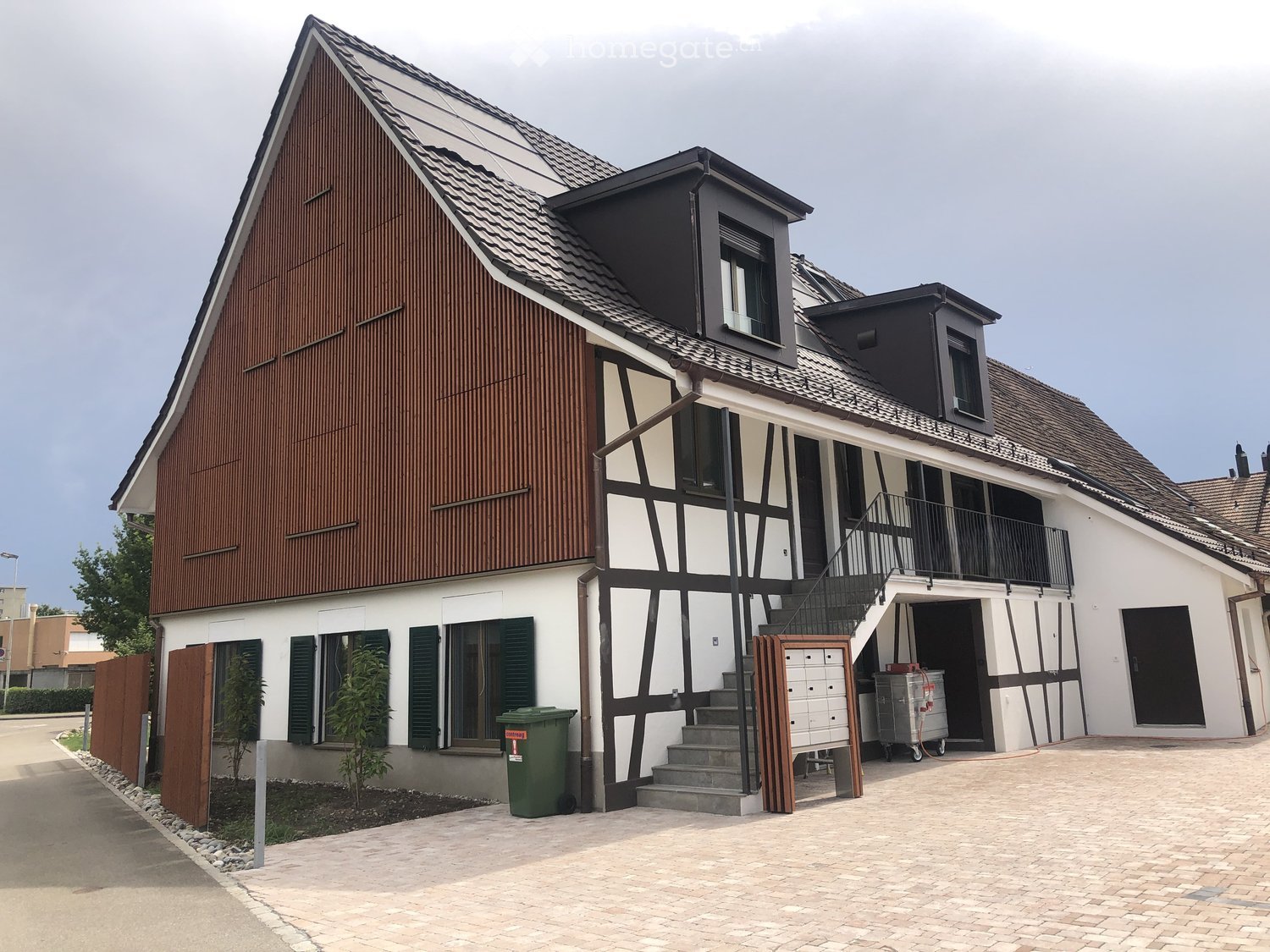 2 story house, brown and white exterior, tiled roof, staircase with railing, balcony, multiple windows, solar panels