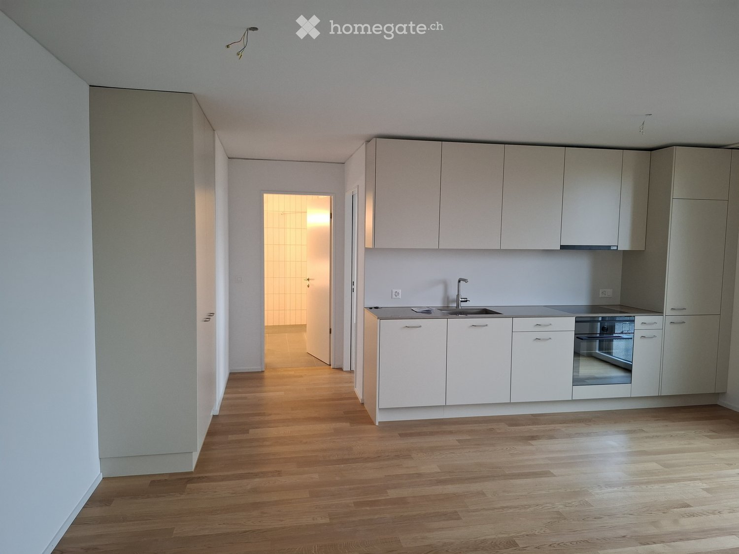 Empty kitchen with white cabinets, stainless steel sink, and wooden flooring. No furniture or appliances are present.