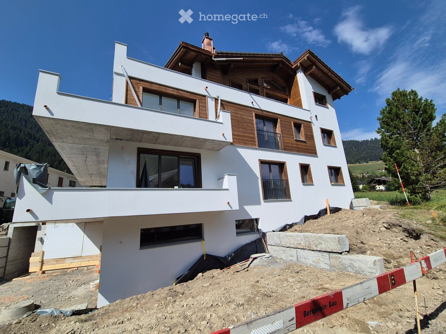 Modern, multi-story house with white walls, wooden accents, and large windows, under construction with exposed scaffolding and construction materials.