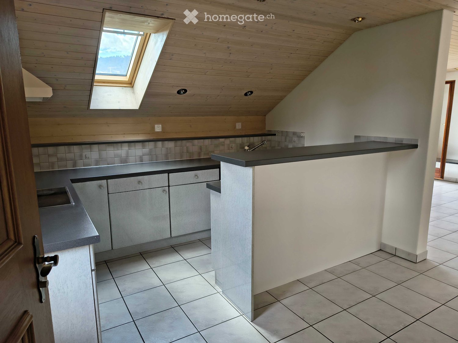 Modern kitchen with light wooden ceiling, tiled backsplash, and white tiled floor. Features built-in cabinets, a sink, and a skylight window.