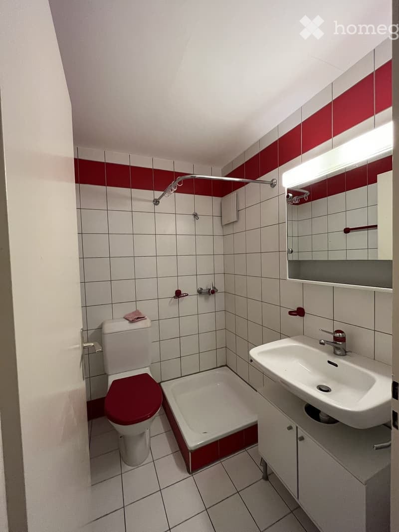 Bathroom with white tiles, red accents, toilet, sink, bathtub, and mirror.