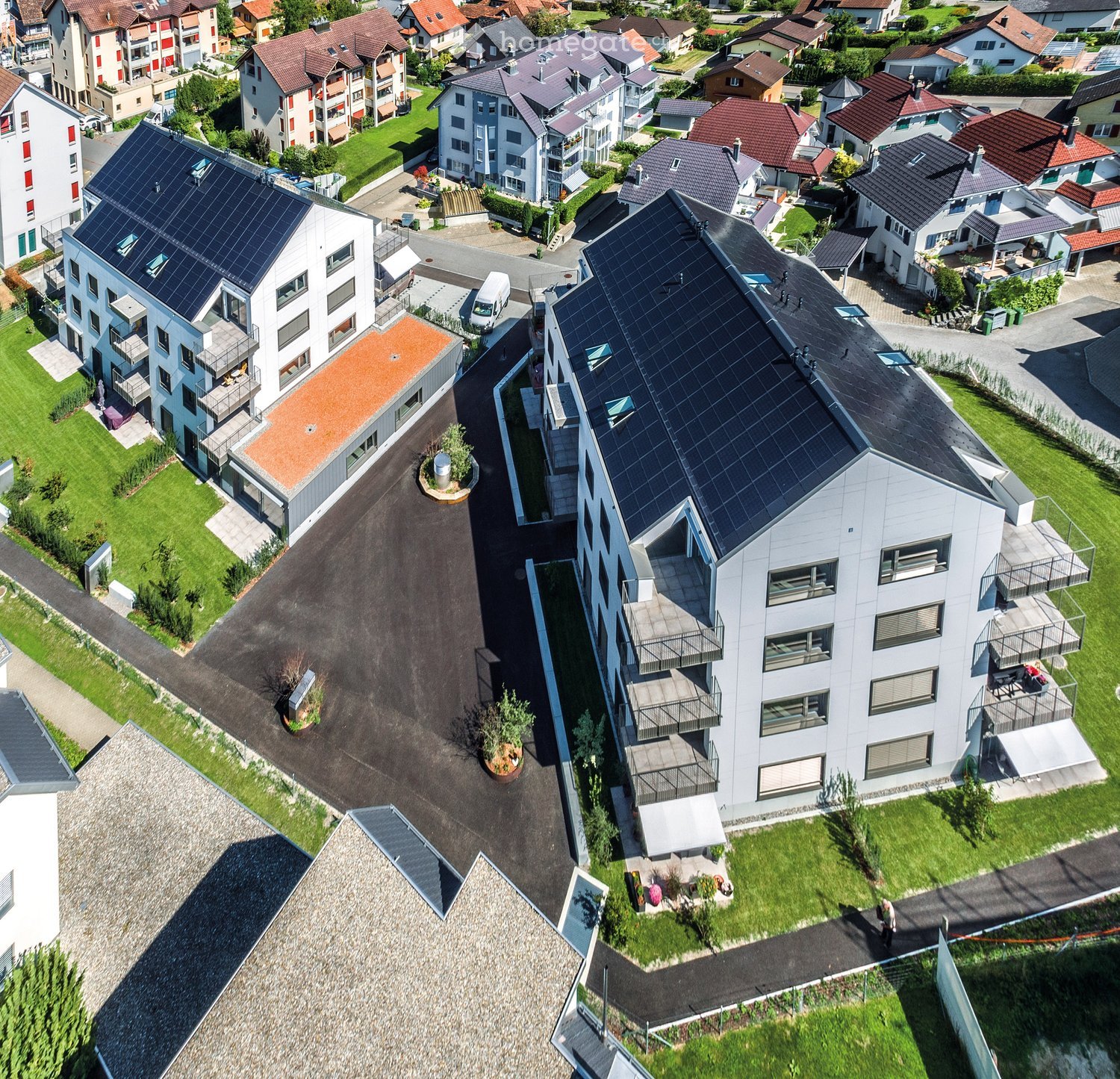 Aerial view of a residential area with multiple modern apartment buildings, green lawns, and solar panels on rooftops.