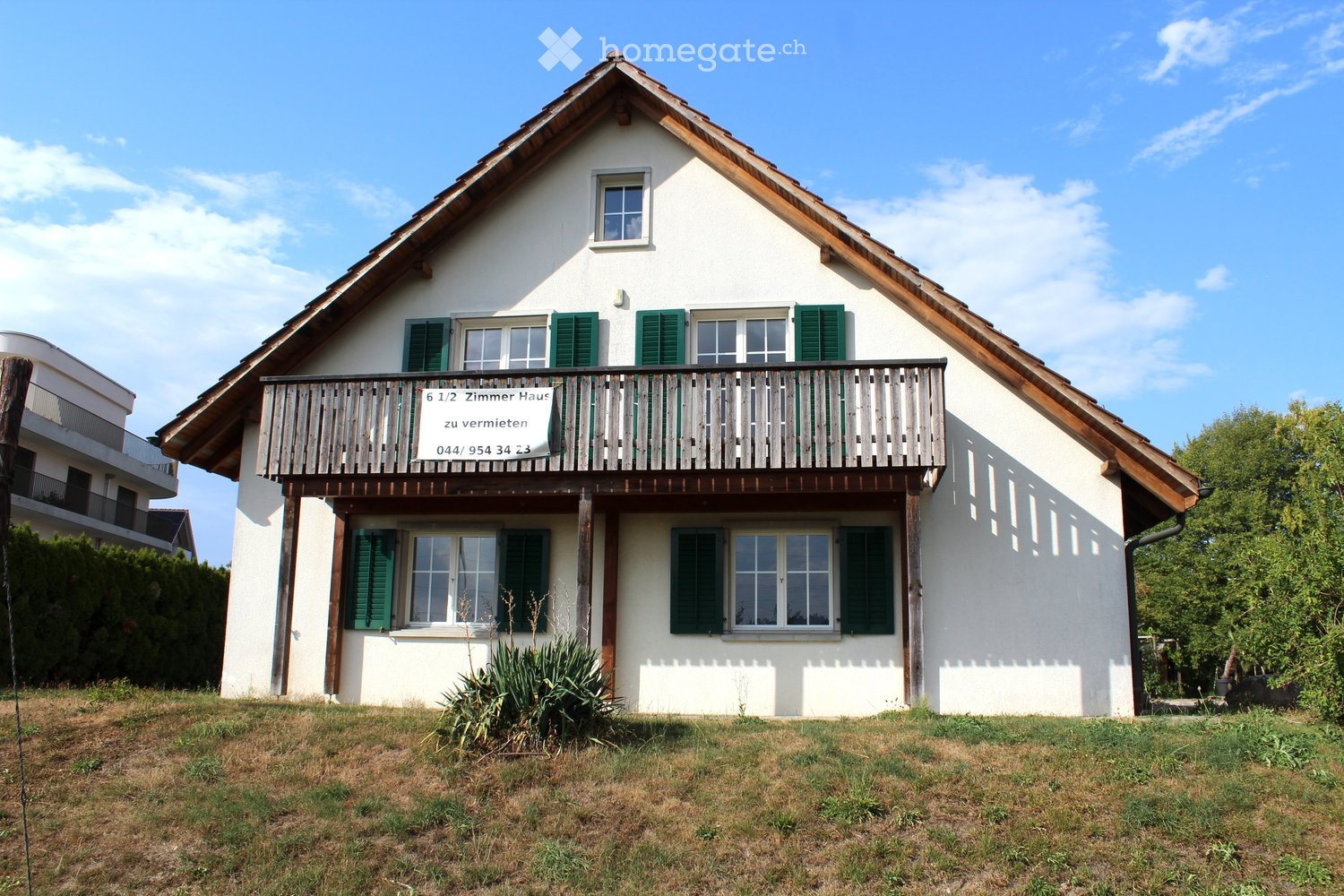 Two-story house with white exterior, green shutters, and a wooden balcony on the upper level.