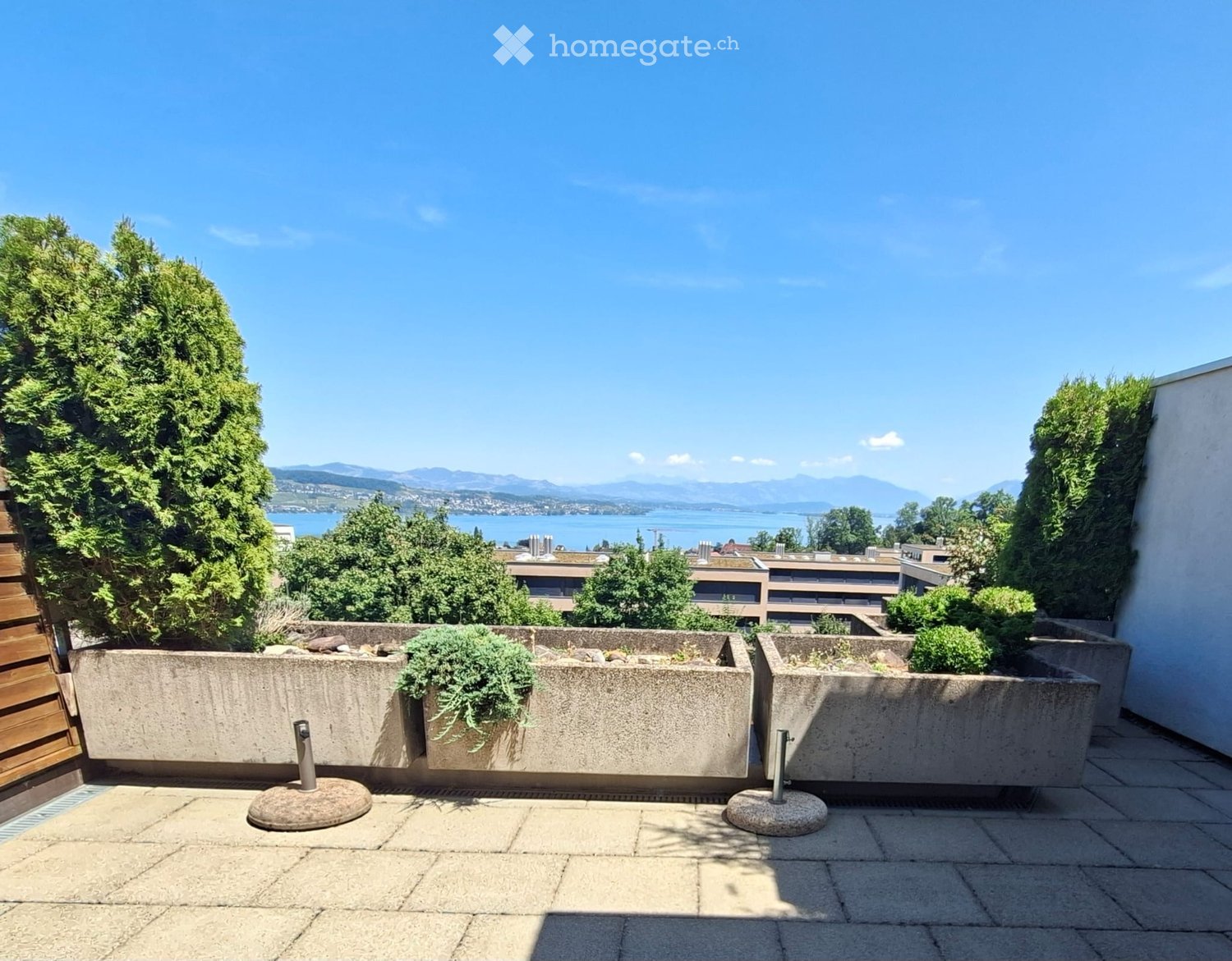 Balcony with concrete planters, tiled floor, and scenic view of a lake and mountains.
