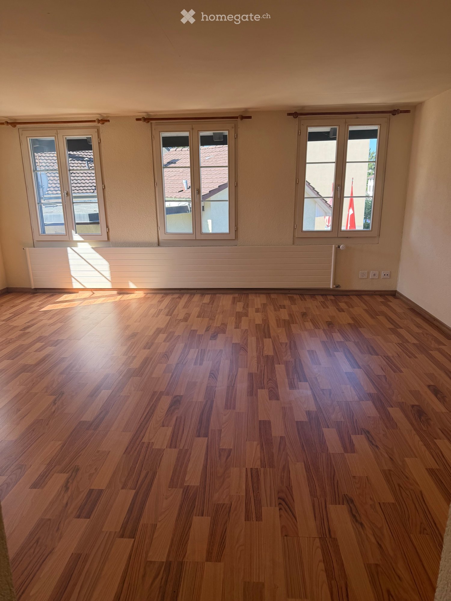 Empty room with wooden flooring, large windows, and radiators. No furniture or equipment present.