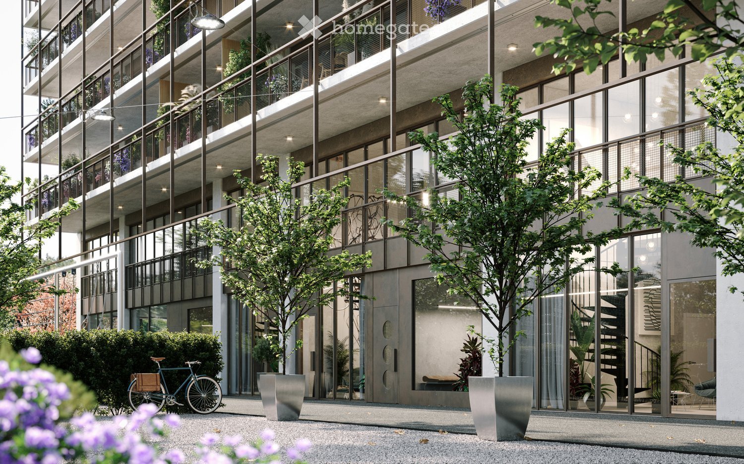 Modern multi-story building with large glass windows and balconies, surrounded by greenery and a bicycle parked nearby.