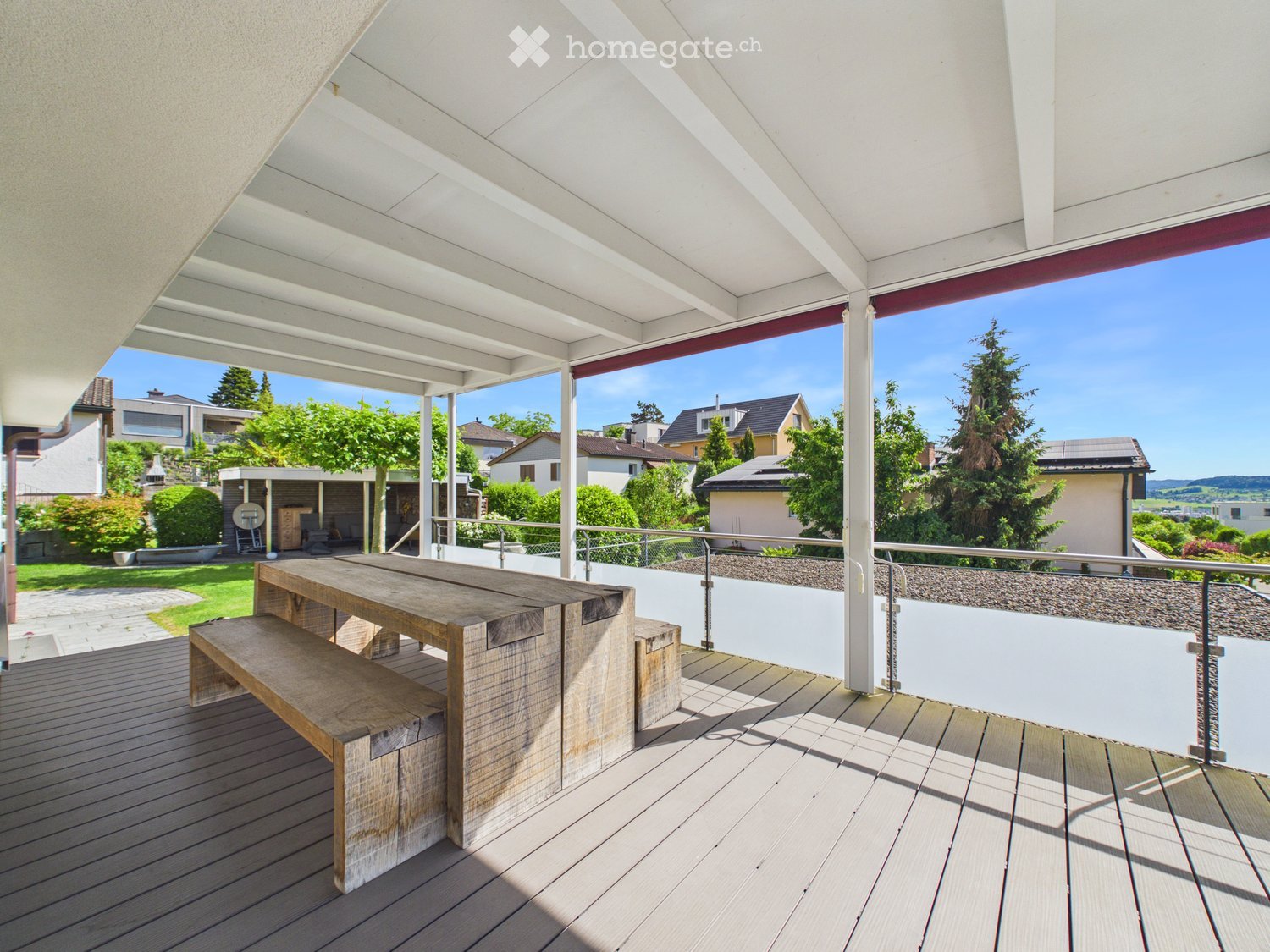 Wooden table and bench on a covered balcony with a view of a suburban neighborhood.