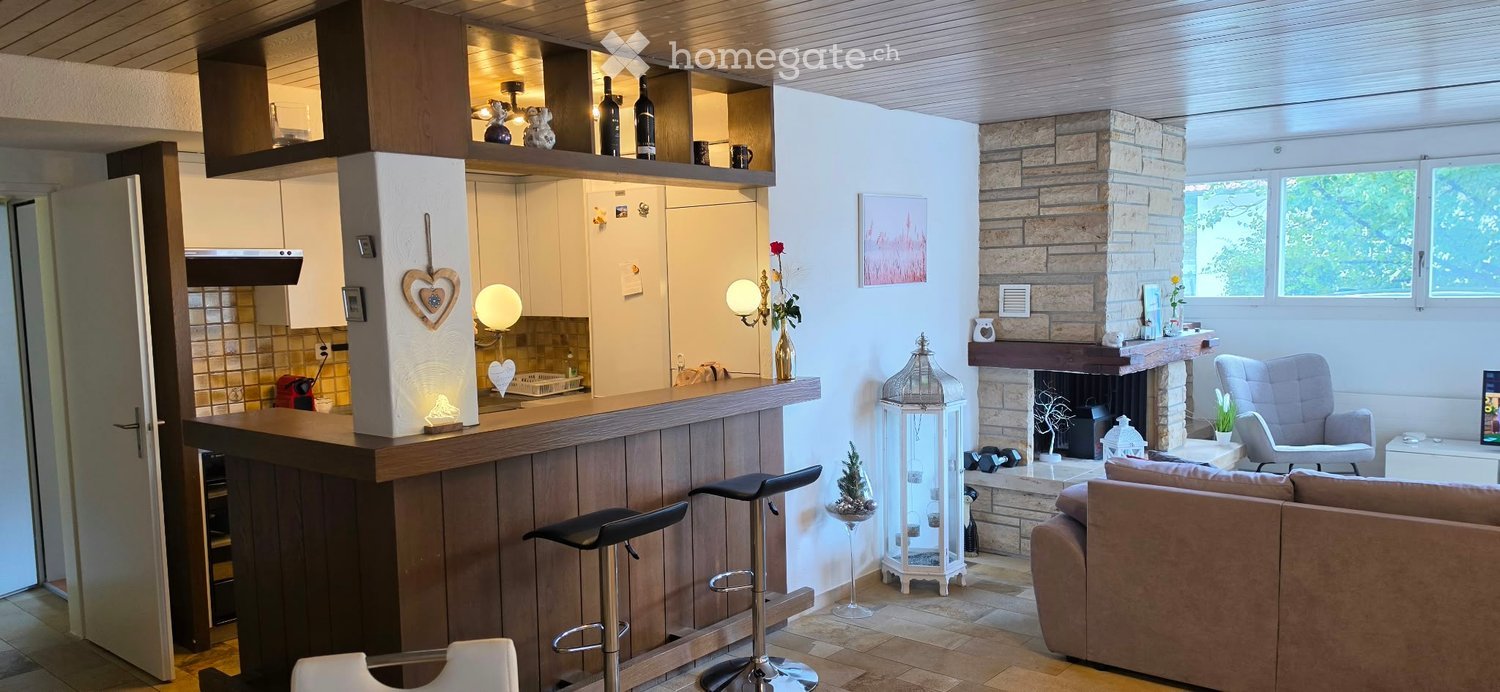 Modern open-plan living and dining area with a stone fireplace, bar counter, sofa, and kitchen cabinets.
