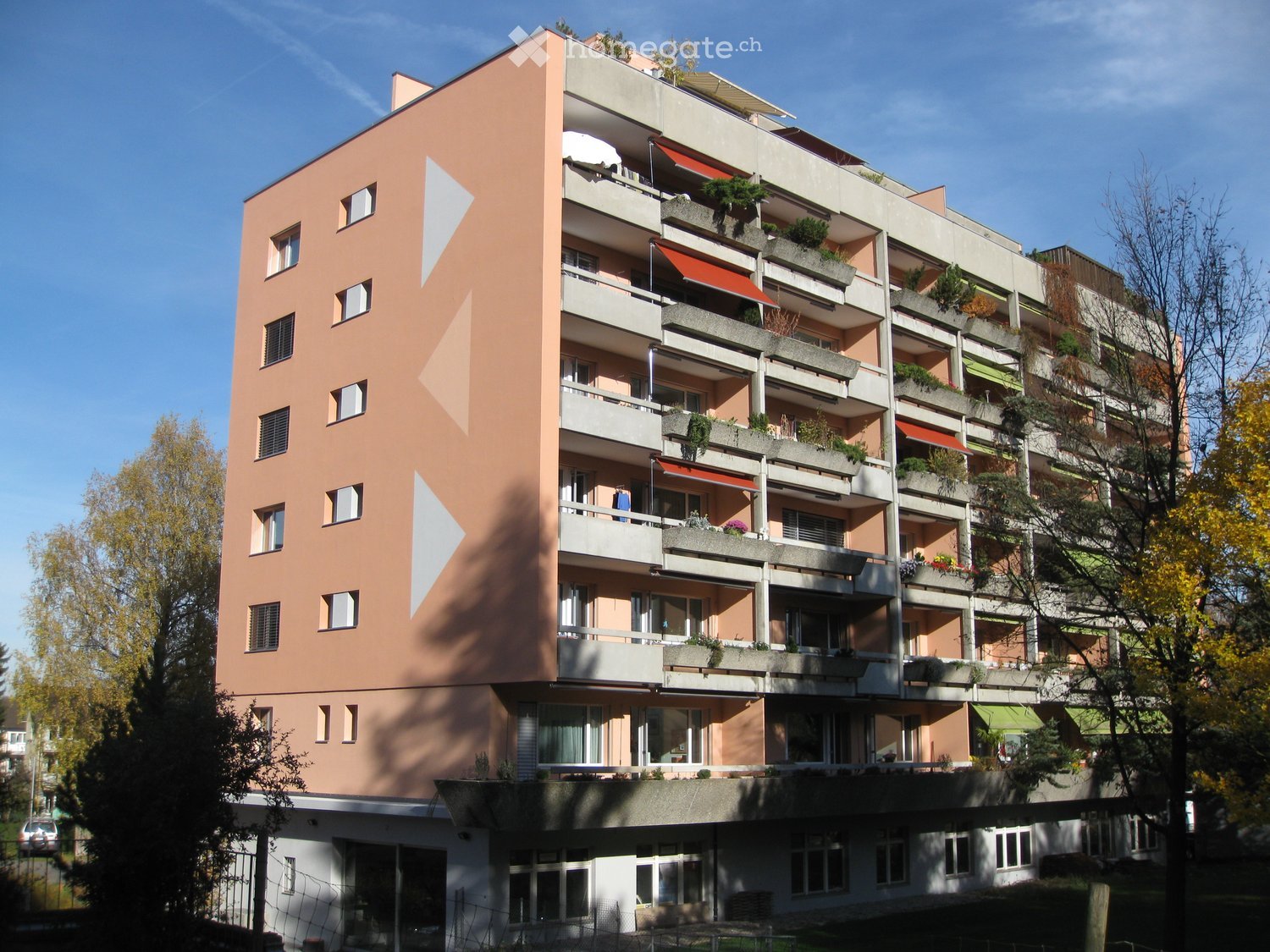 Multi-story residential building with balconies, greenery, and modern design.