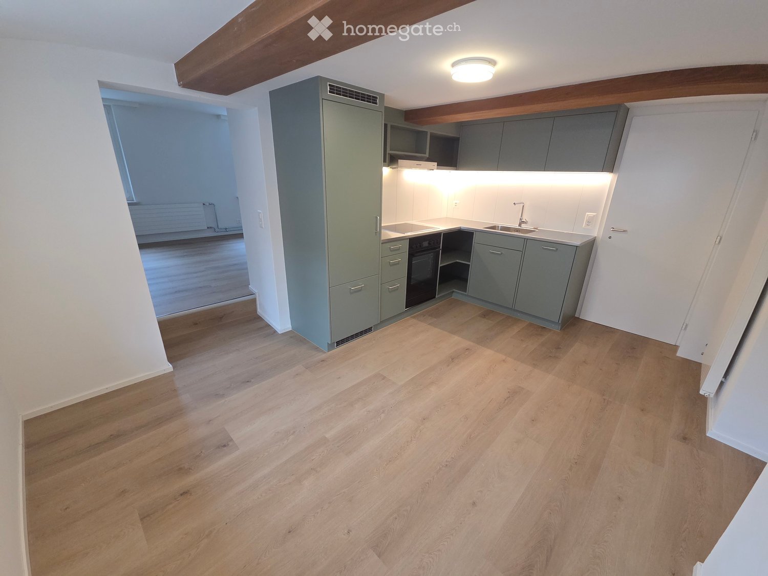Modern kitchen with grey cabinets, wooden flooring, and built-in appliances including a sink, faucet, and oven. The space is well-lit with recessed lighting and has exposed wooden beams on the ceiling.