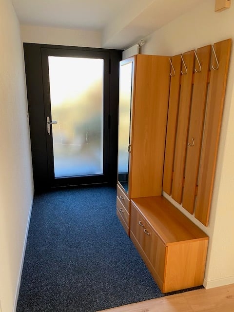 Hallway with a wooden bench and coat rack, leading to a black door with a glass panel.
