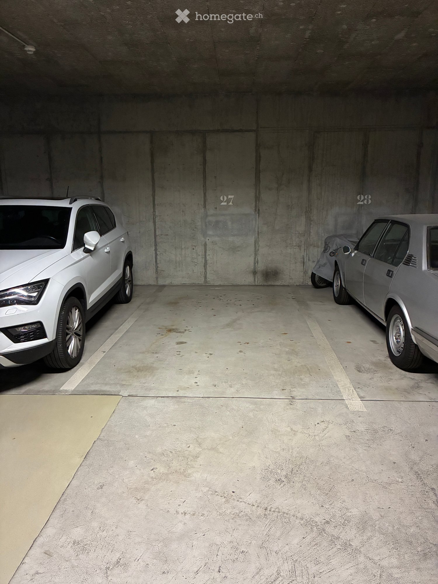 Underground parking area with two parked cars, marked parking spaces numbered 27 and 28, and a concrete floor.