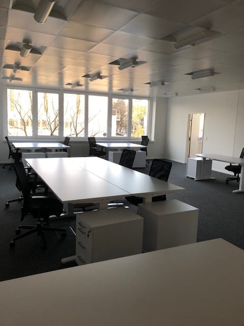 Bright, modern office space with large windows, white tables, black chairs, and gray cabinets.