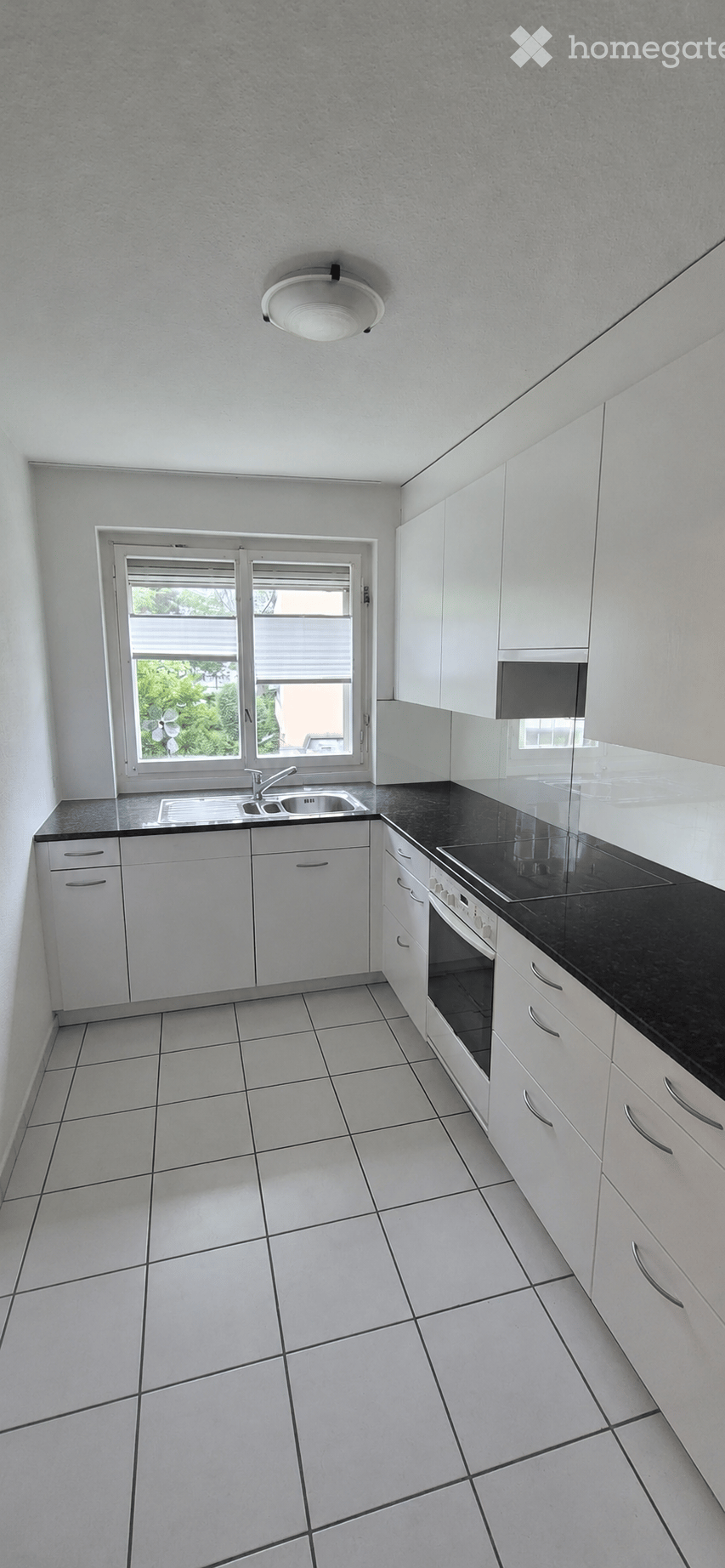 Modern kitchen with white cabinets, black countertops, tiled floor, and a window above the sink.