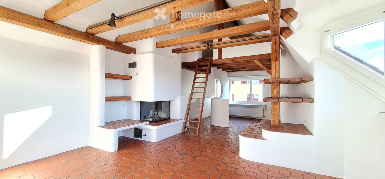 Living room with exposed wooden beams, brick floor, fireplace, built-in benches, and wooden shelves.