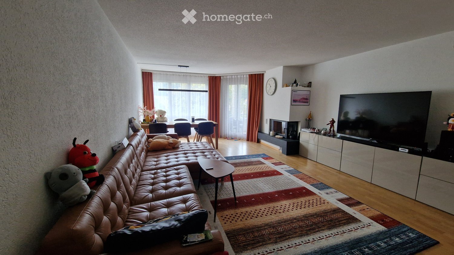 Modern living room with a leather sofa, coffee table, flat-screen TV, dining area with chairs, fireplace, and decorative items.