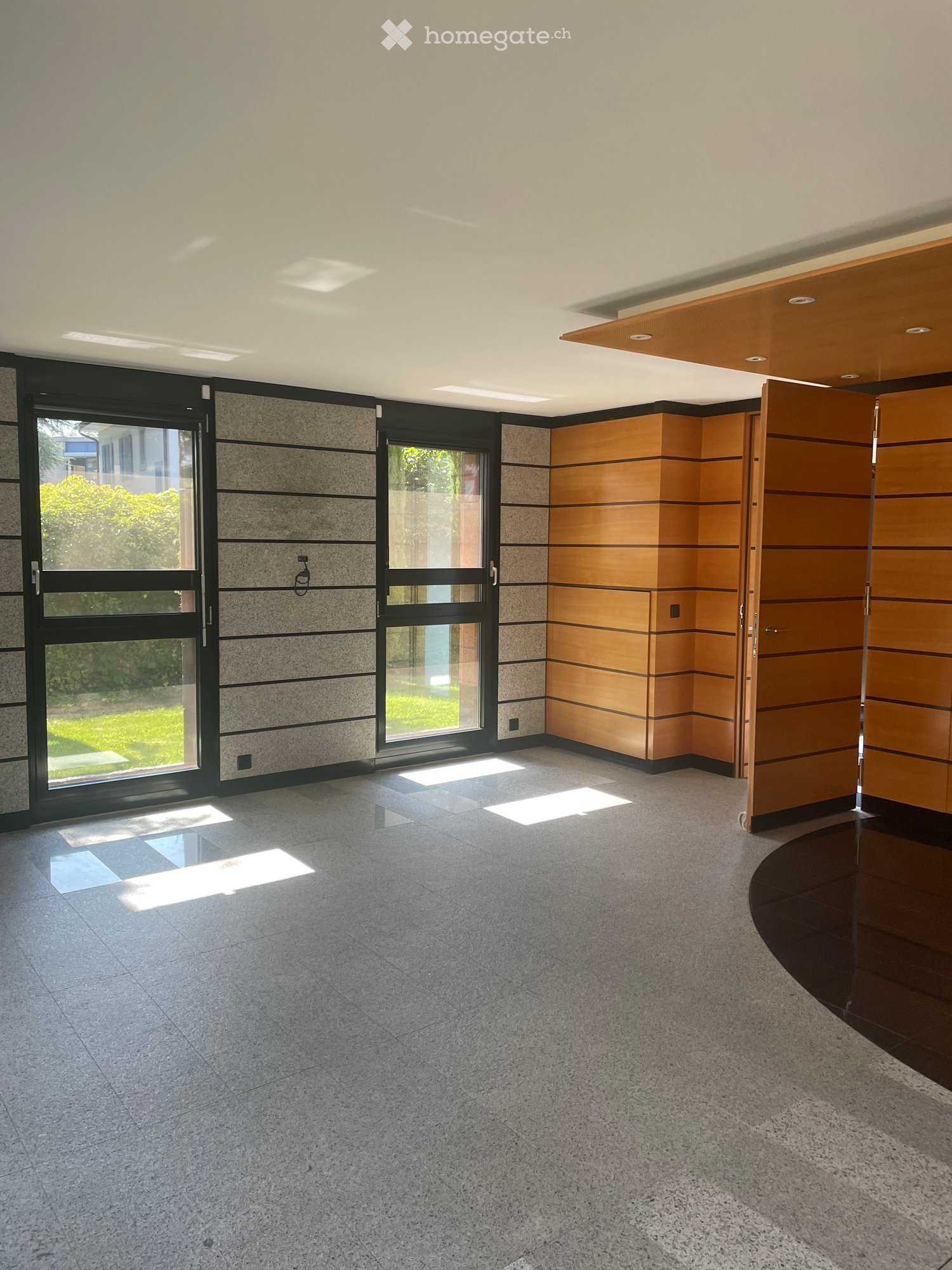 Empty room with modern design, large windows, polished concrete floor, and wooden paneling on one wall.