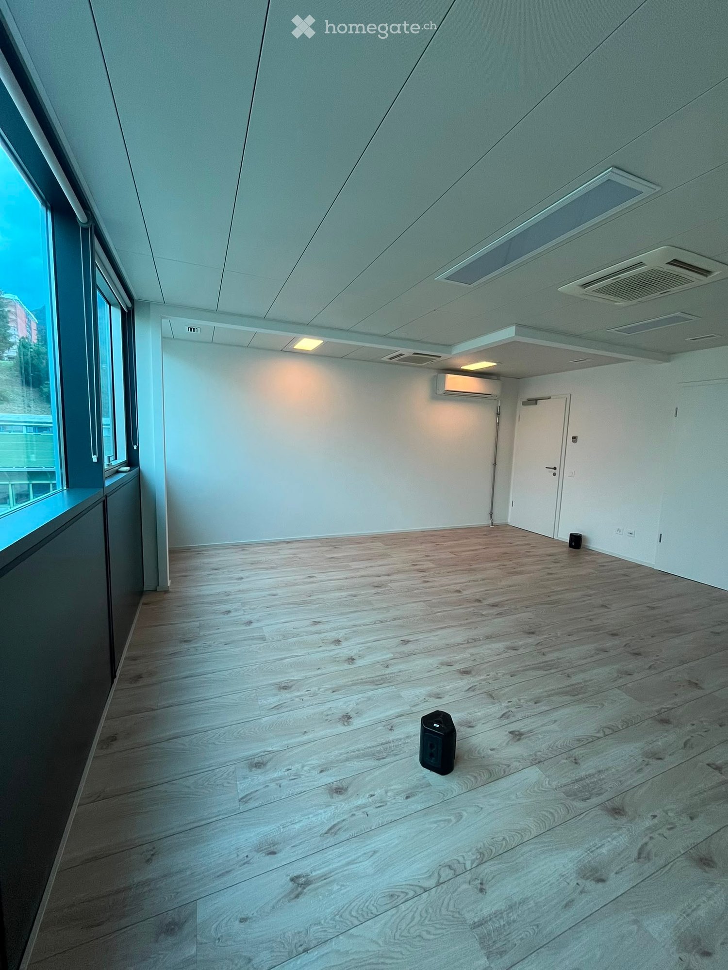 Empty room with wooden flooring, white walls, large windows, and a white door.