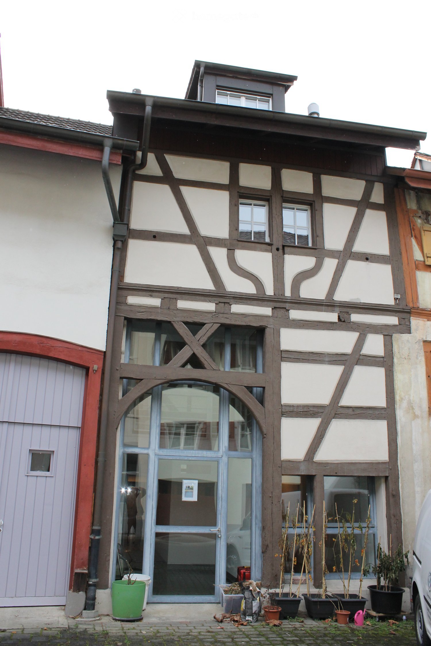 Traditional half-timbered house with white plaster and dark wooden beams, featuring a large arched entrance and multiple windows.