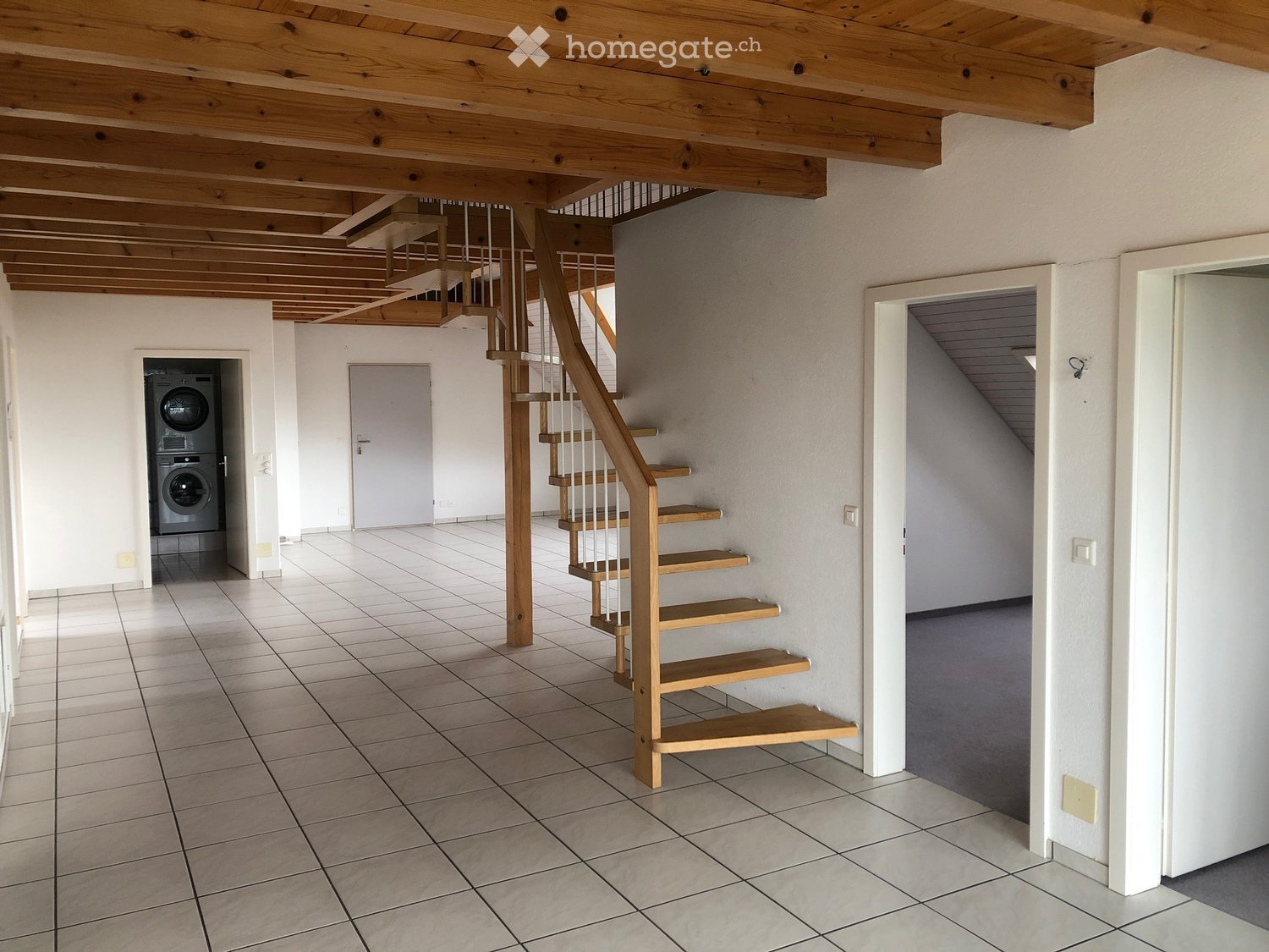 Spacious hallway with wooden staircase, tiled floor, and a washing machine in the background.