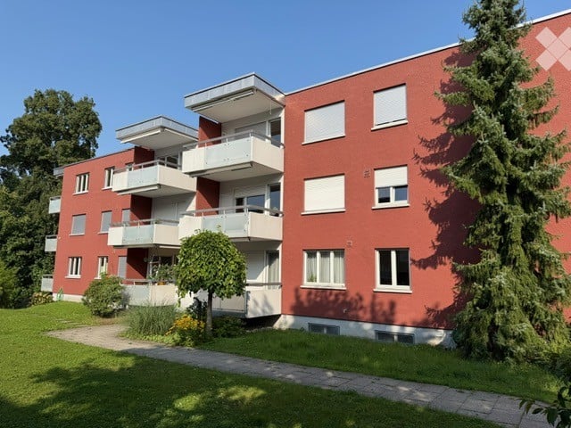 Red brick apartment building with multiple balconies and a well-maintained lawn in front.
