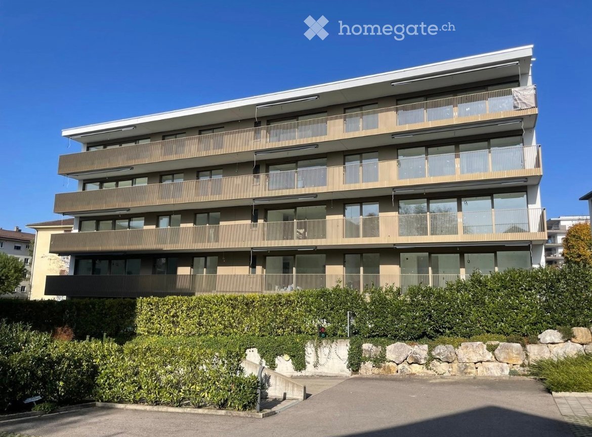 Modern multi-story residential building with balconies, large windows, and a landscaped garden area.