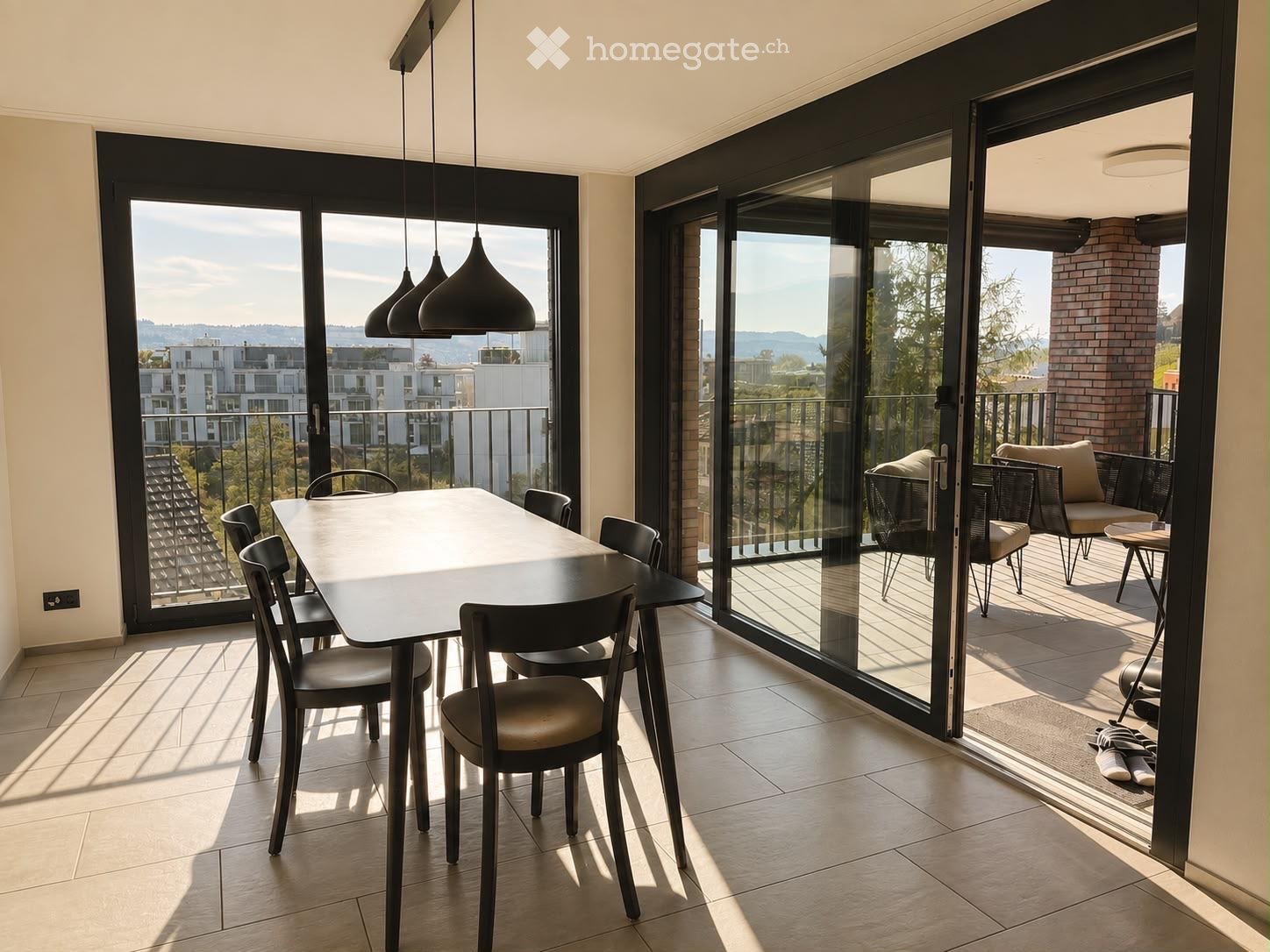 Modern dining area with a sleek black dining table and chairs, large sliding glass doors opening to a balcony with outdoor seating, and a scenic city view.
