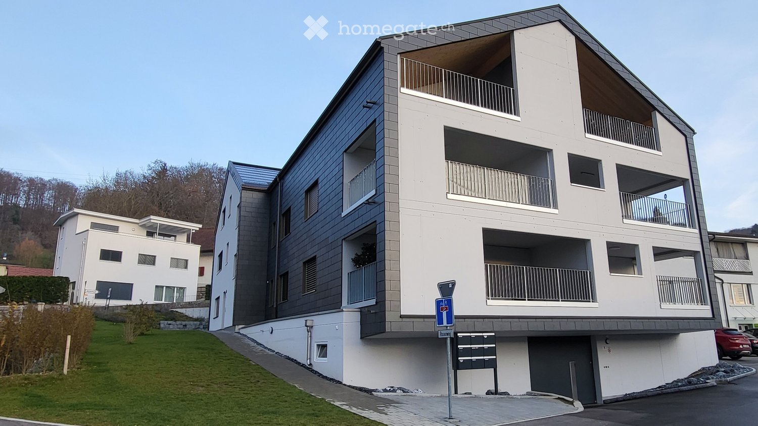 Modern multi-story residential building with balconies, grey and white facade, and a raised ground floor entrance.