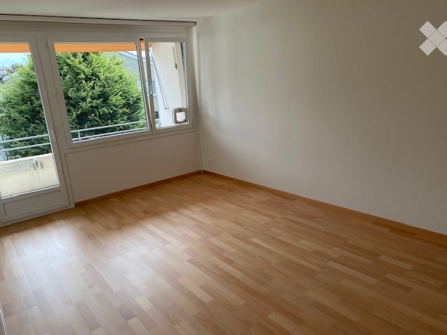Empty room with wooden flooring, large windows, and a balcony access door.