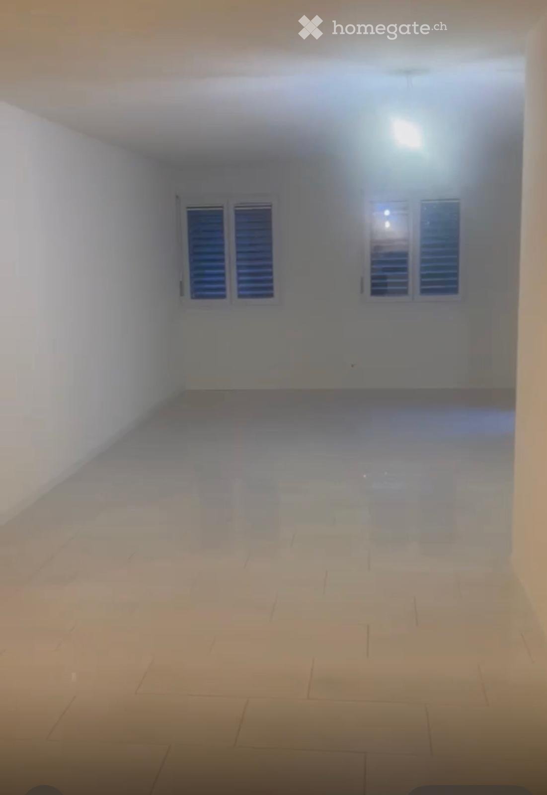 Empty room with white walls, tiled floor, and two windows with shutters.