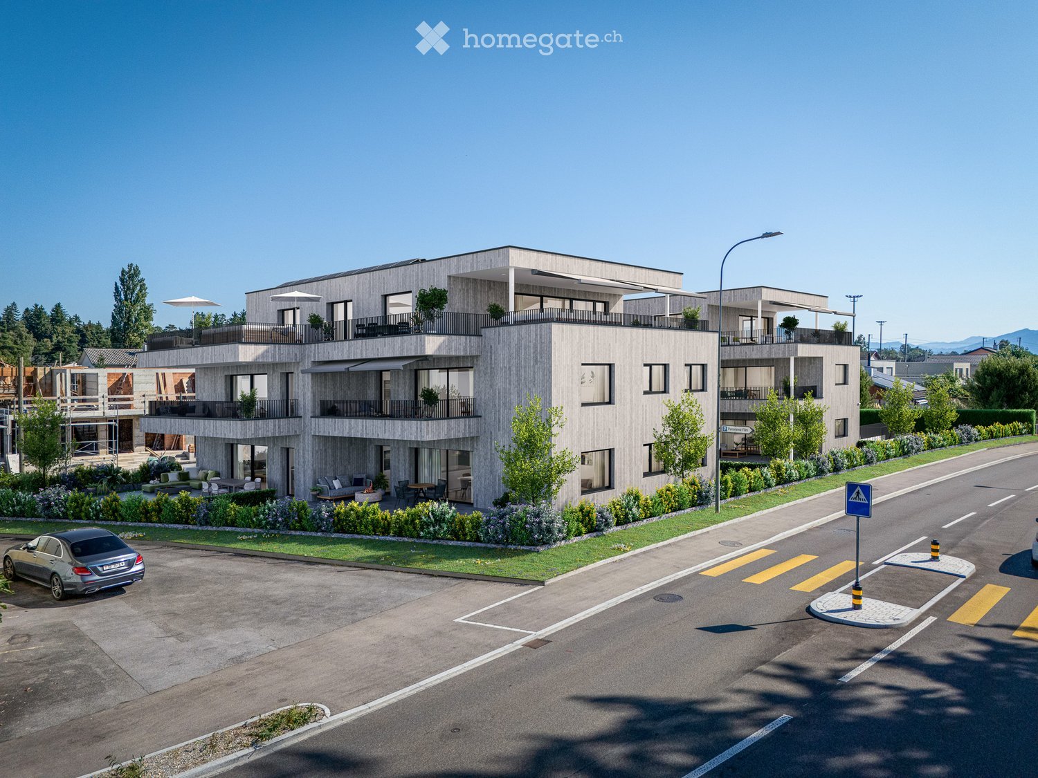 Modern multi-story building with balconies, surrounded by greenery and a parking lot.