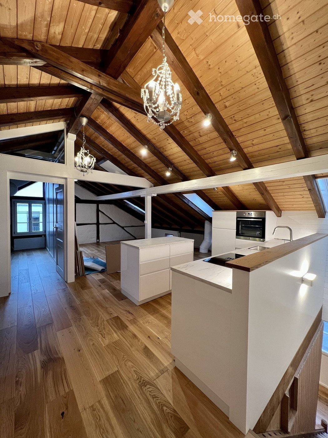 Modern kitchen with wooden floors, white cabinets, a central island, and exposed wooden beams on the ceiling.