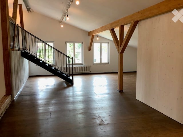 Spacious room with hardwood floor, wooden beams, stairs, windows