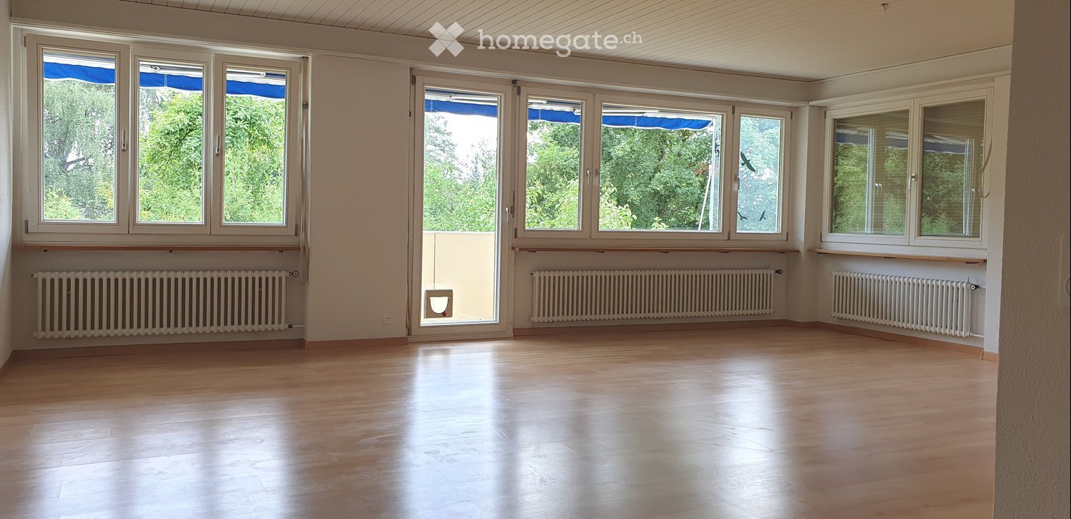Empty room with wooden flooring, large windows, radiators, and a door leading to a balcony.