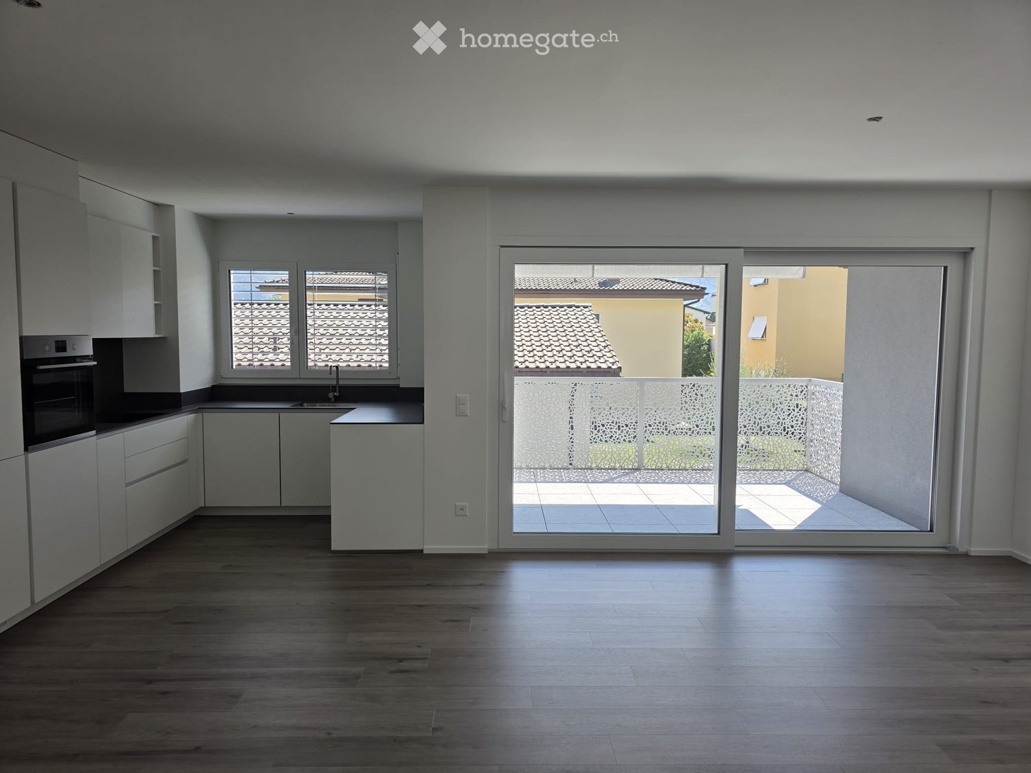 Empty kitchen with white cabinets, dark countertops, and a large sliding glass door leading to a balcony.