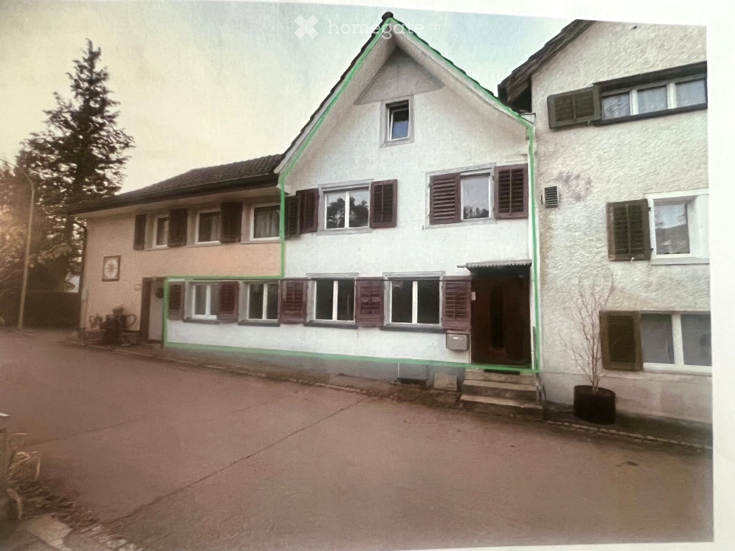 Two-story house with white exterior, multiple windows with shutters, and a small garden area with potted plants.
