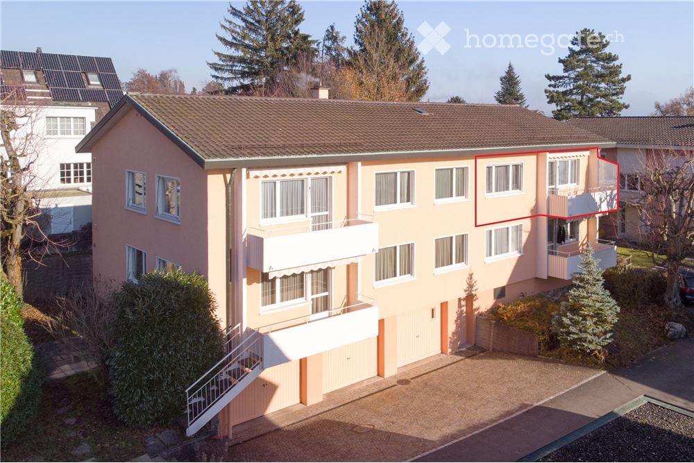 Two-story residential building with pink facade, multiple windows, balconies, and a garage entrance.