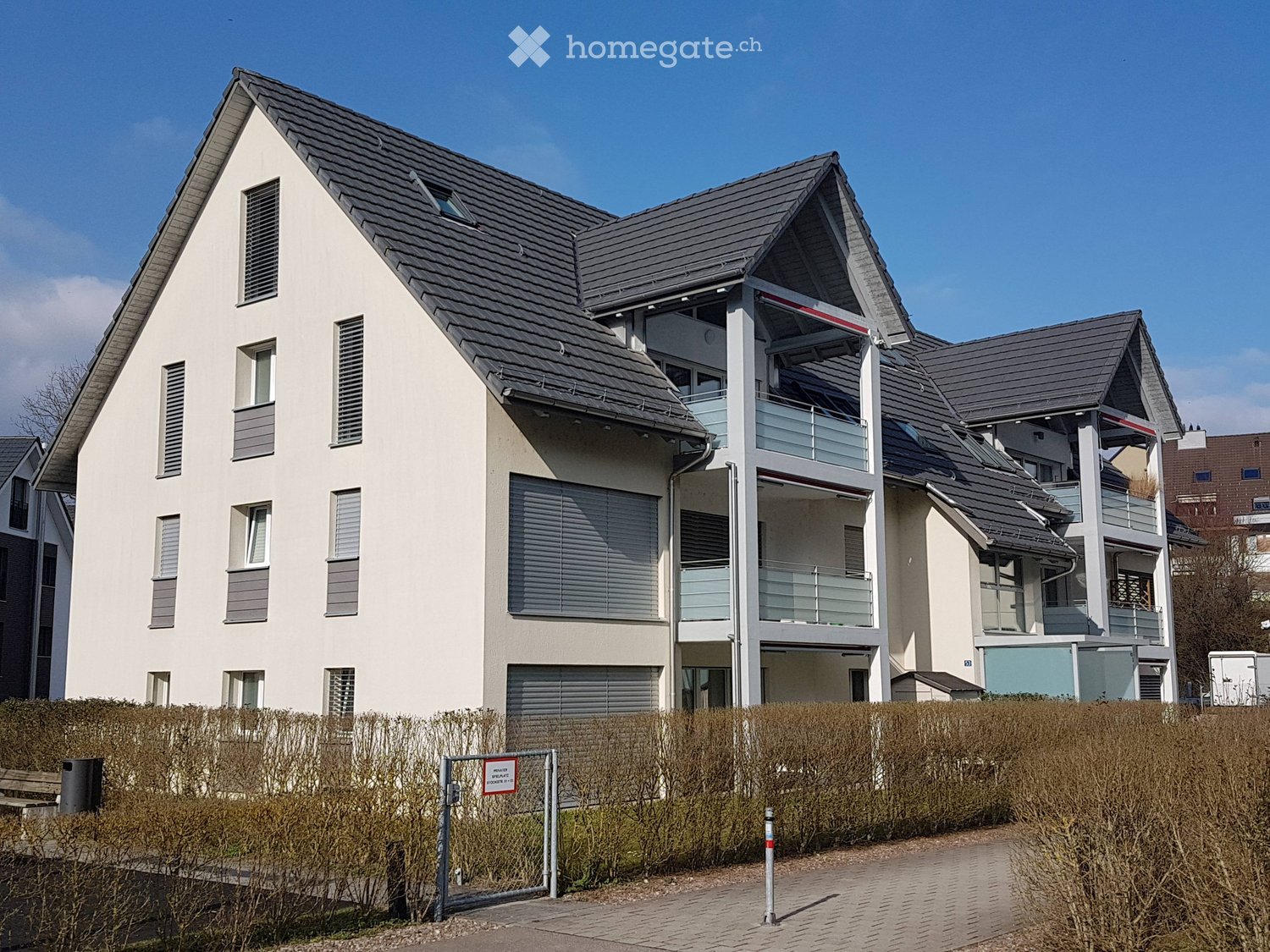 Modern two-story house with grey roof, white walls, multiple windows, and a balcony on the upper level.