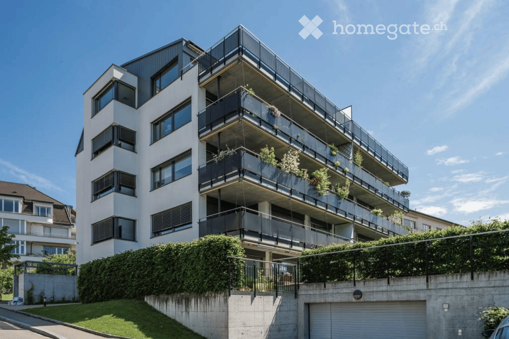 Modern multi-story apartment building with balconies, large windows, and greenery on the lower level.